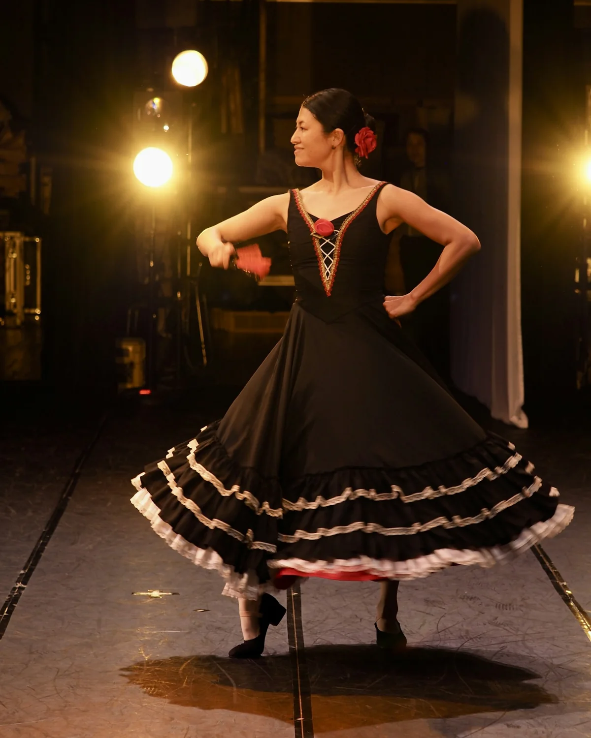 A flamenco dancer in a black and white ruffled dress, mid-turn on a lit stage with a red flower in her hair (representative photograph of a flamenco performance, not El Palacio Andaluz)