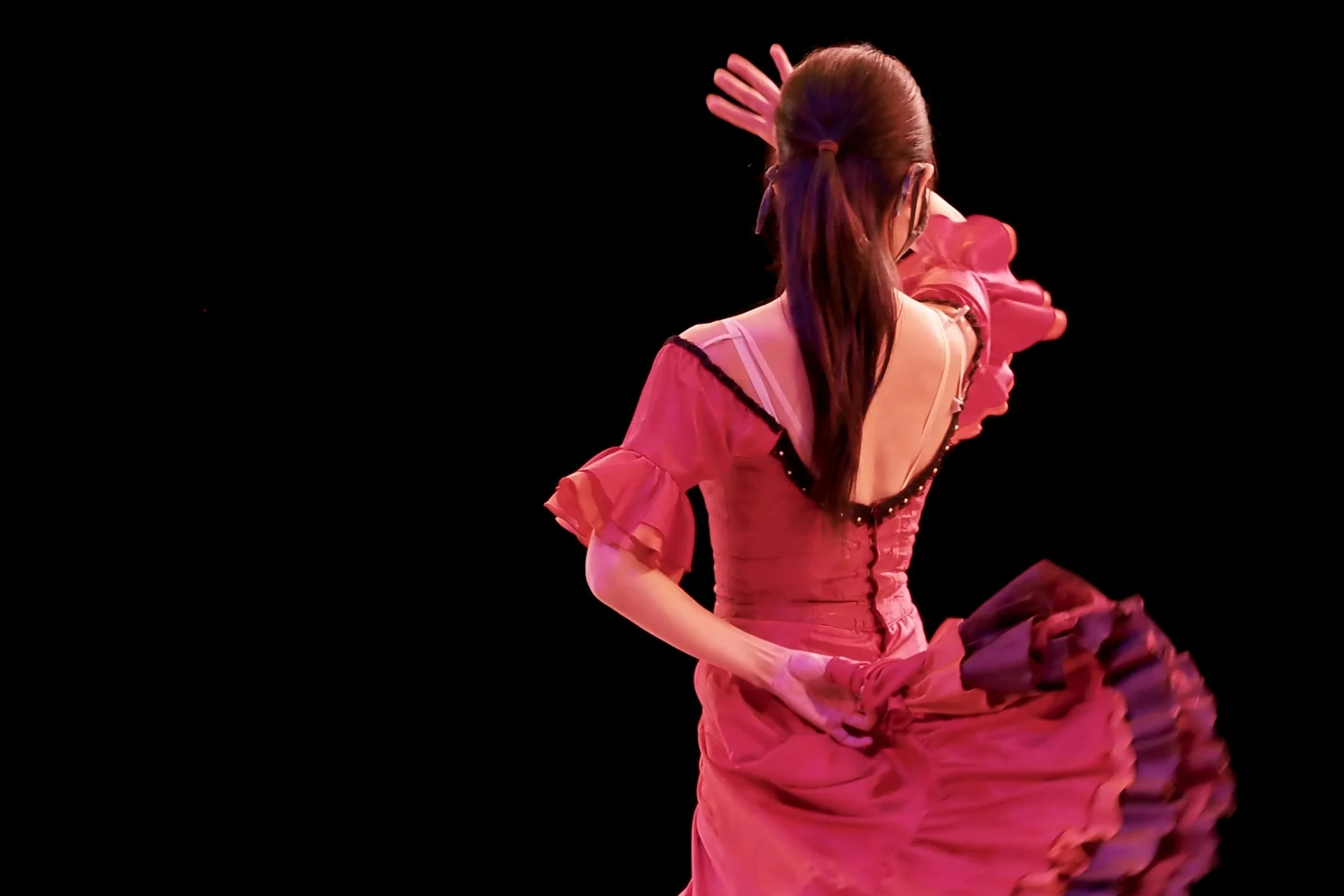 A flamenco dancer mid-turn in a pink ruffled dress on a dark stage, skirt lifted in motion (representative photograph of a flamenco performance, not El Palacio Andaluz itself)